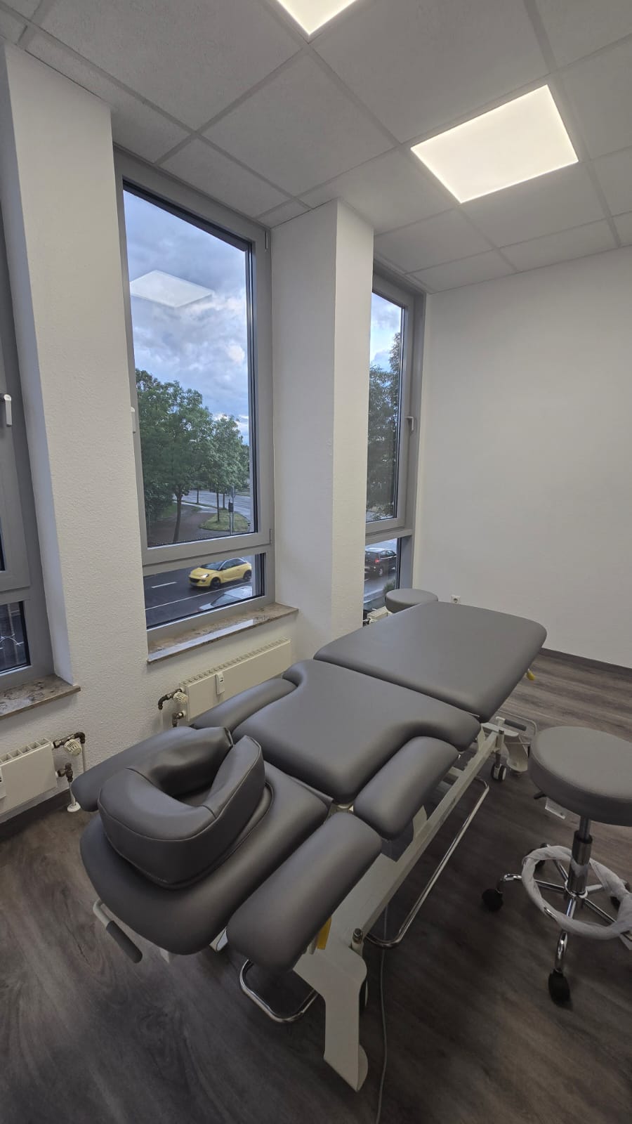 Behandlungsraum mit Therapieliege und großen Fenstern.